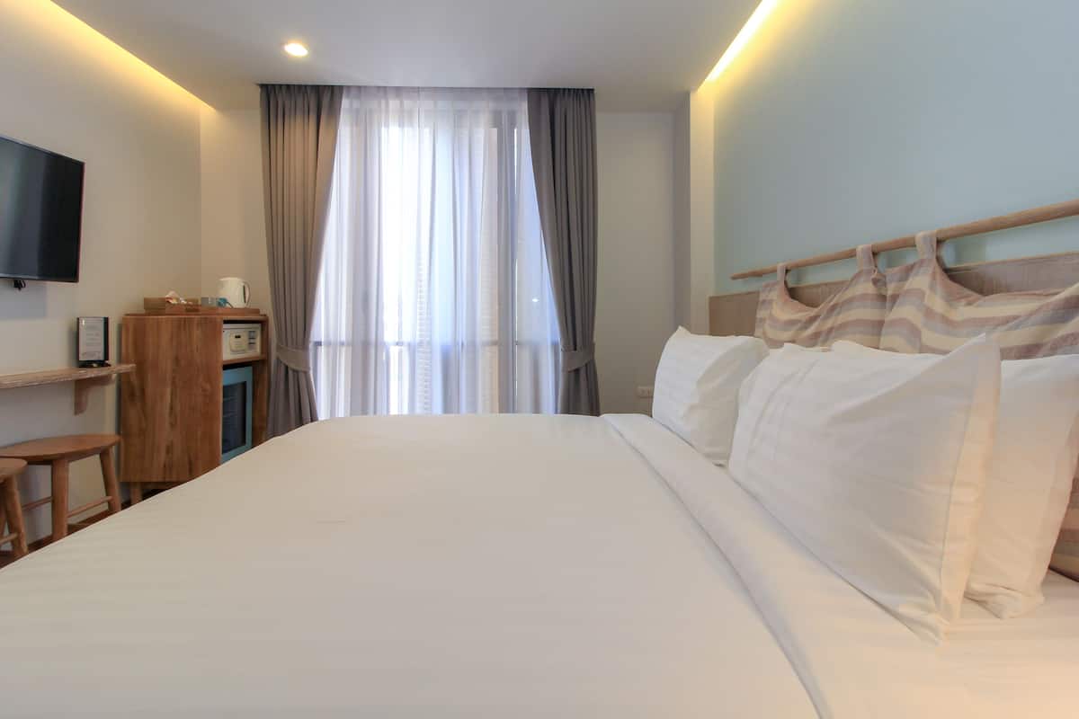 Une chambre d’hôtel avec un grand lit, un téléviseur fixé au mur, un bureau avec une chaise et une fenêtre avec des rideaux.