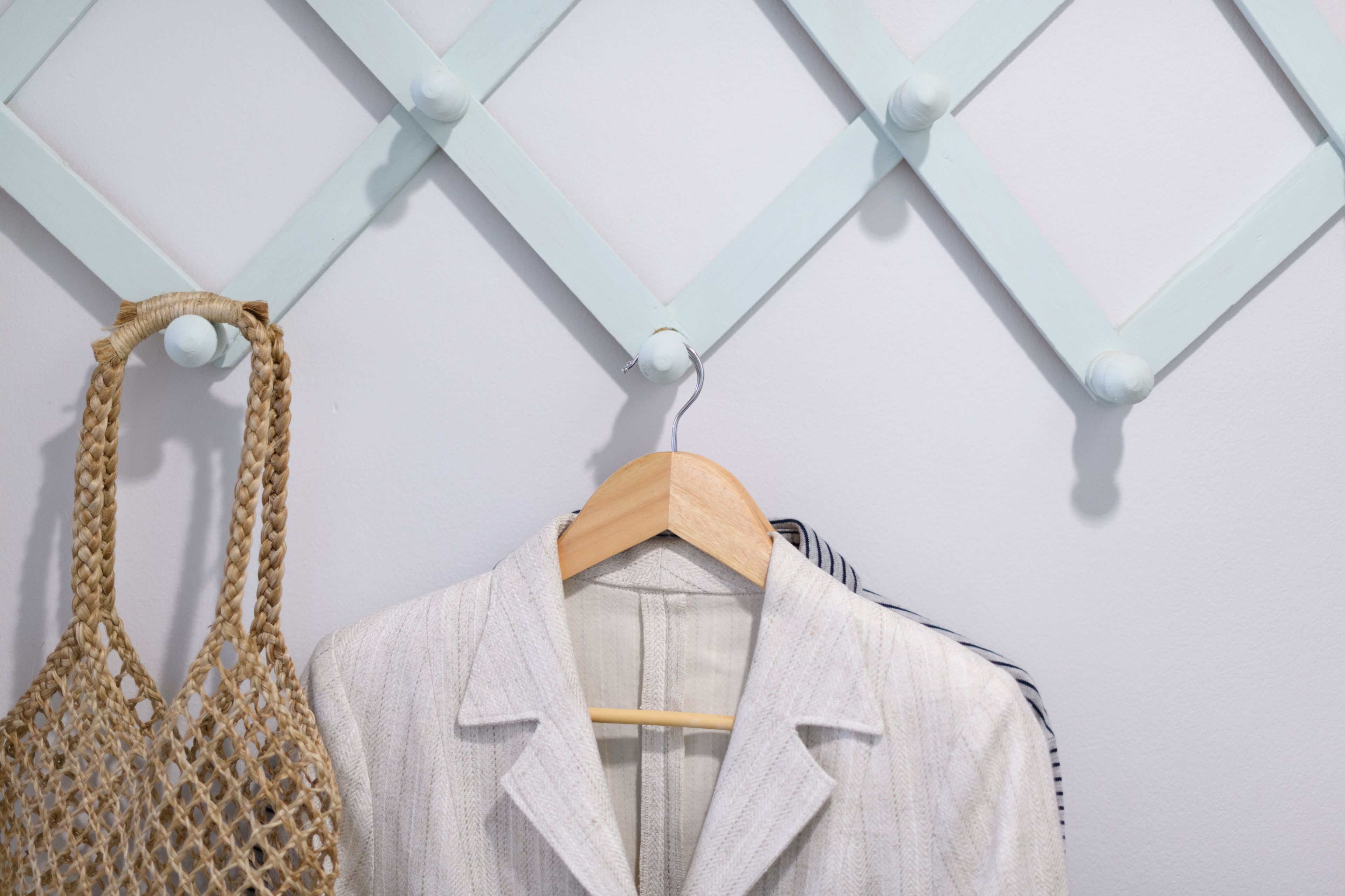 Une blouse blanche est suspendue à un cintre en bois devant un mur bleu clair orné d’un motif géométrique.