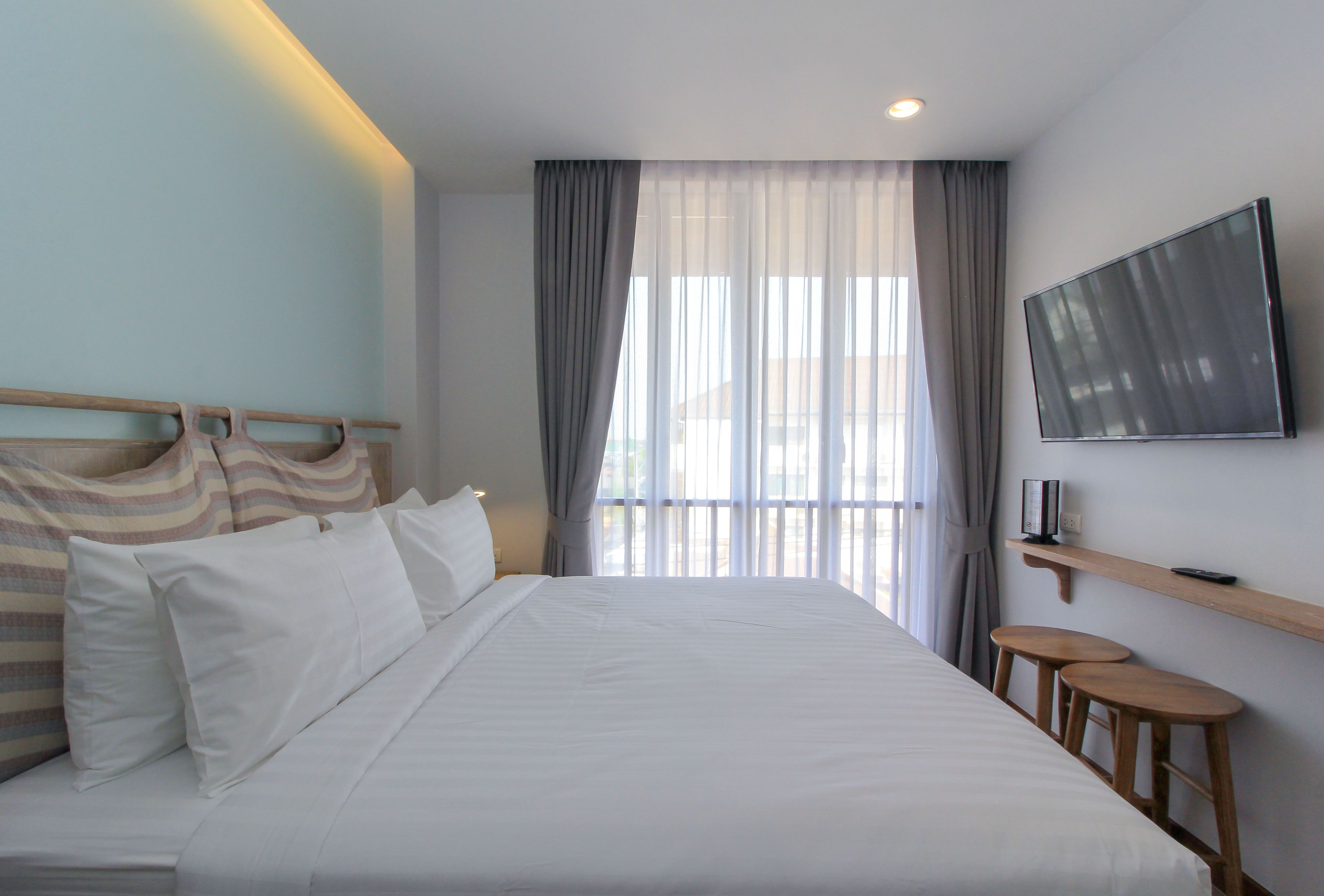 Una habitación de hotel con una cama grande, un televisor montado en la pared y una ventana con cortinas.