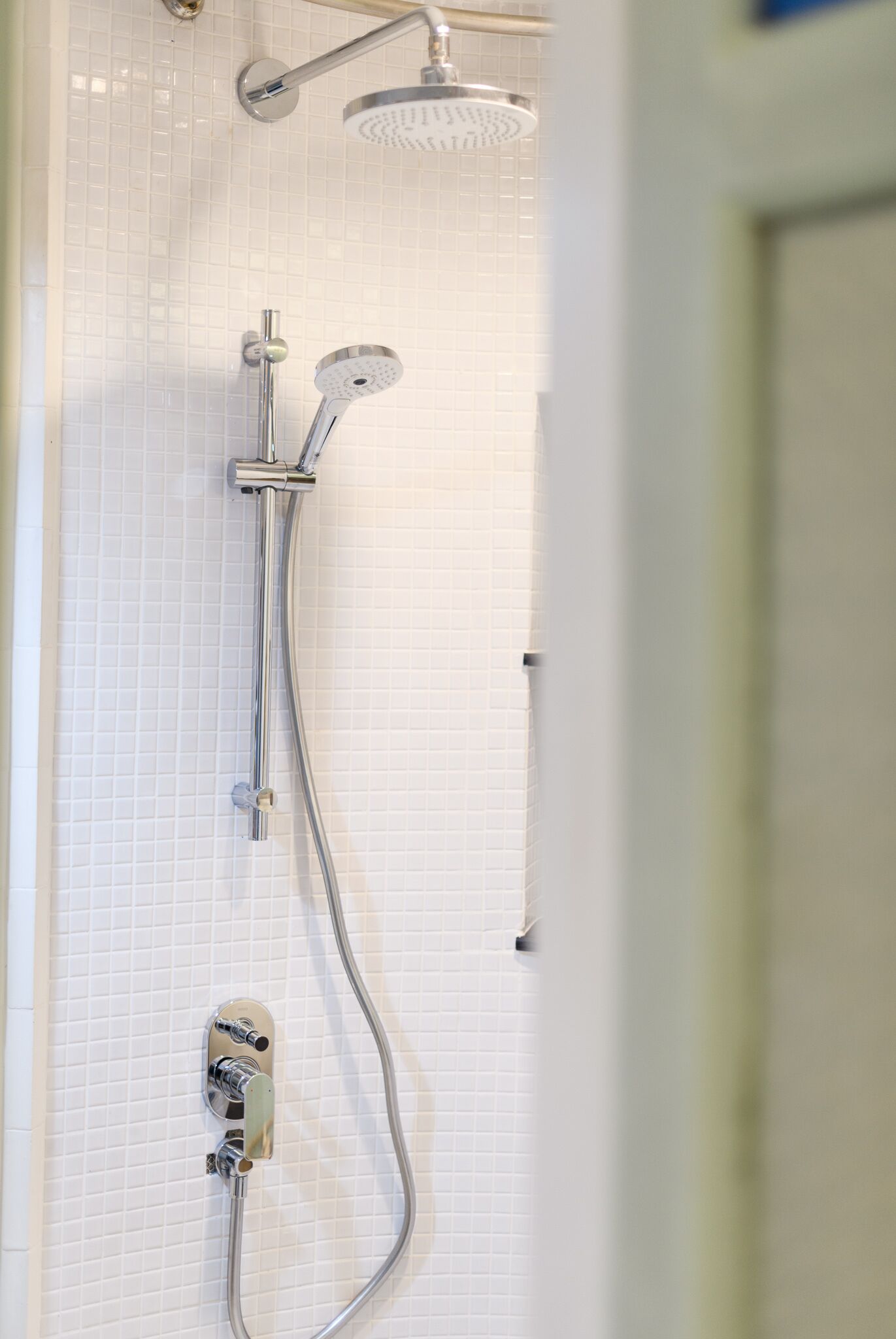 A shower with a handheld showerhead and a wall-mounted control panel.