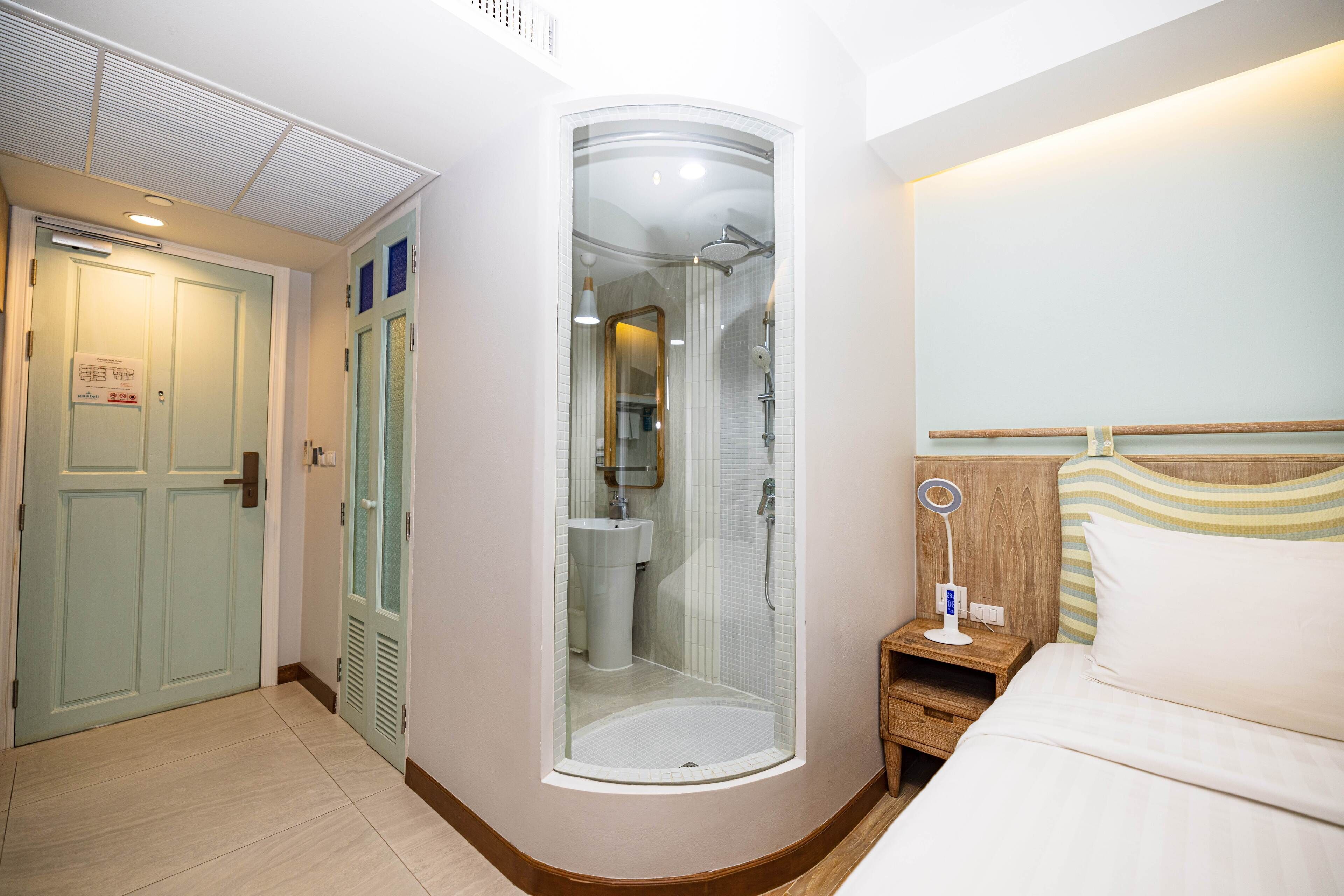 A hotel room with a shower, a bedside table, a bed, and a door.