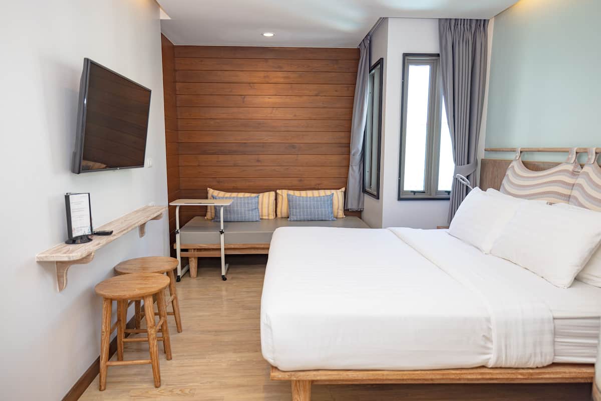 Une chambre d’hôtel avec un grand lit, un petit coin salon, un téléviseur fixé au mur et une fenêtre avec des rideaux.