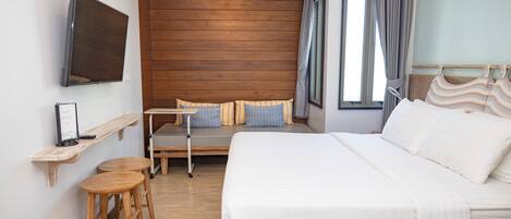 Habitación de hotel con una cama grande, un rincón de descanso, un televisor montado en la pared y una ventana con cortinas.