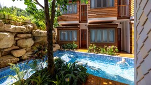 Un immeuble à plusieurs étages doté d’une piscine, entouré de plantes et bordé d’un mur en pierre.