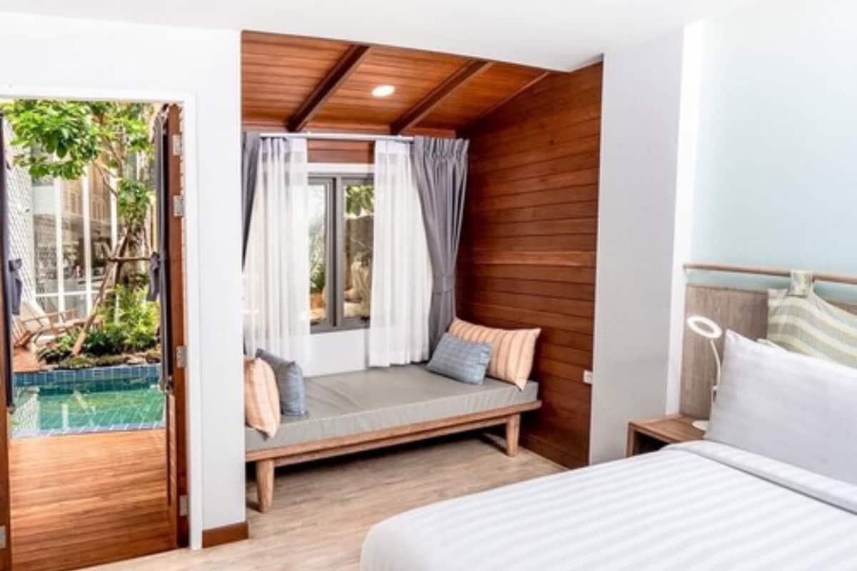 Une chambre avec un plafond en bois, un lit, une table de chevet et une fenêtre avec des rideaux.