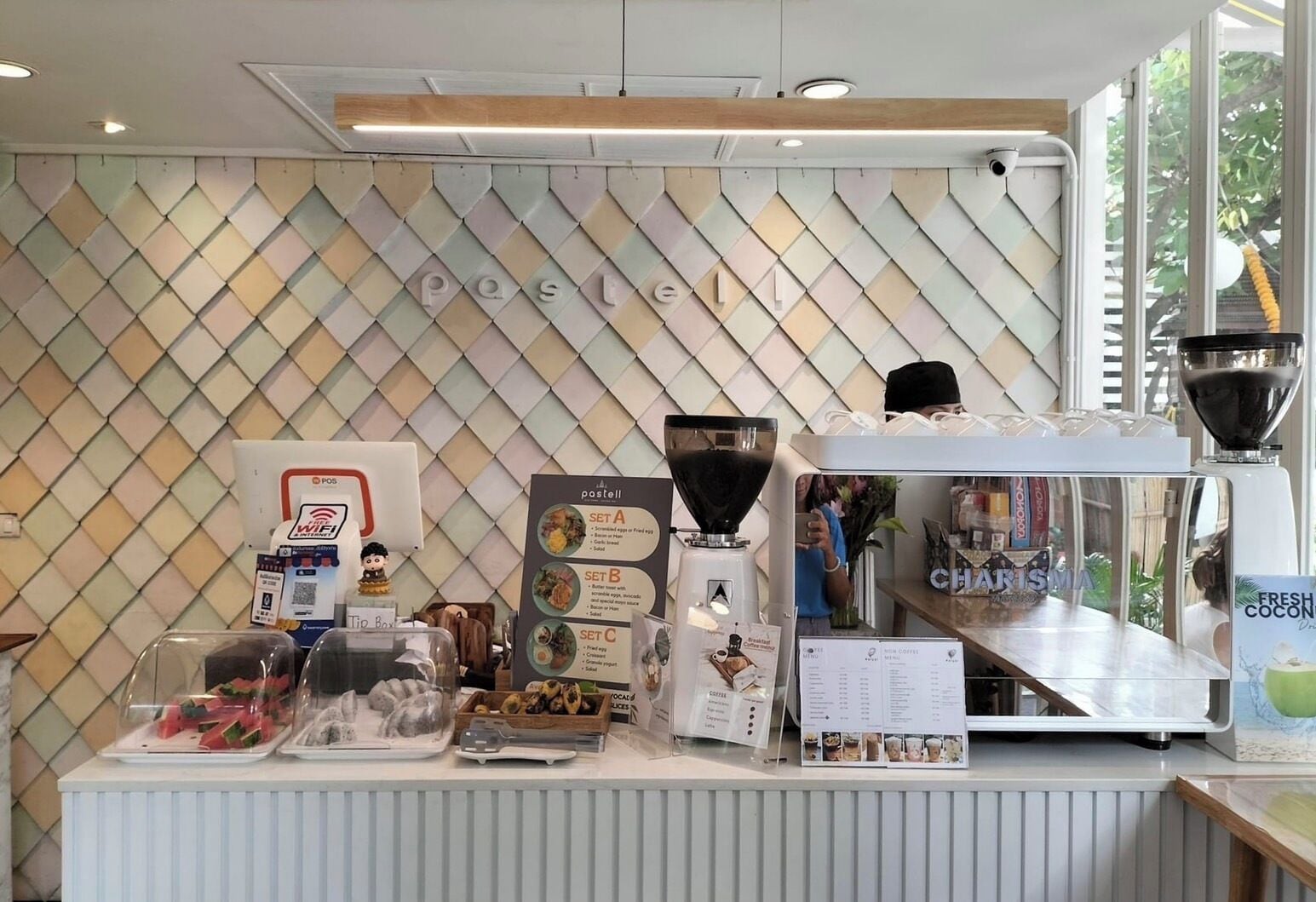 A coffee shop counter with a menu board, a coffee machine, and a tip box.