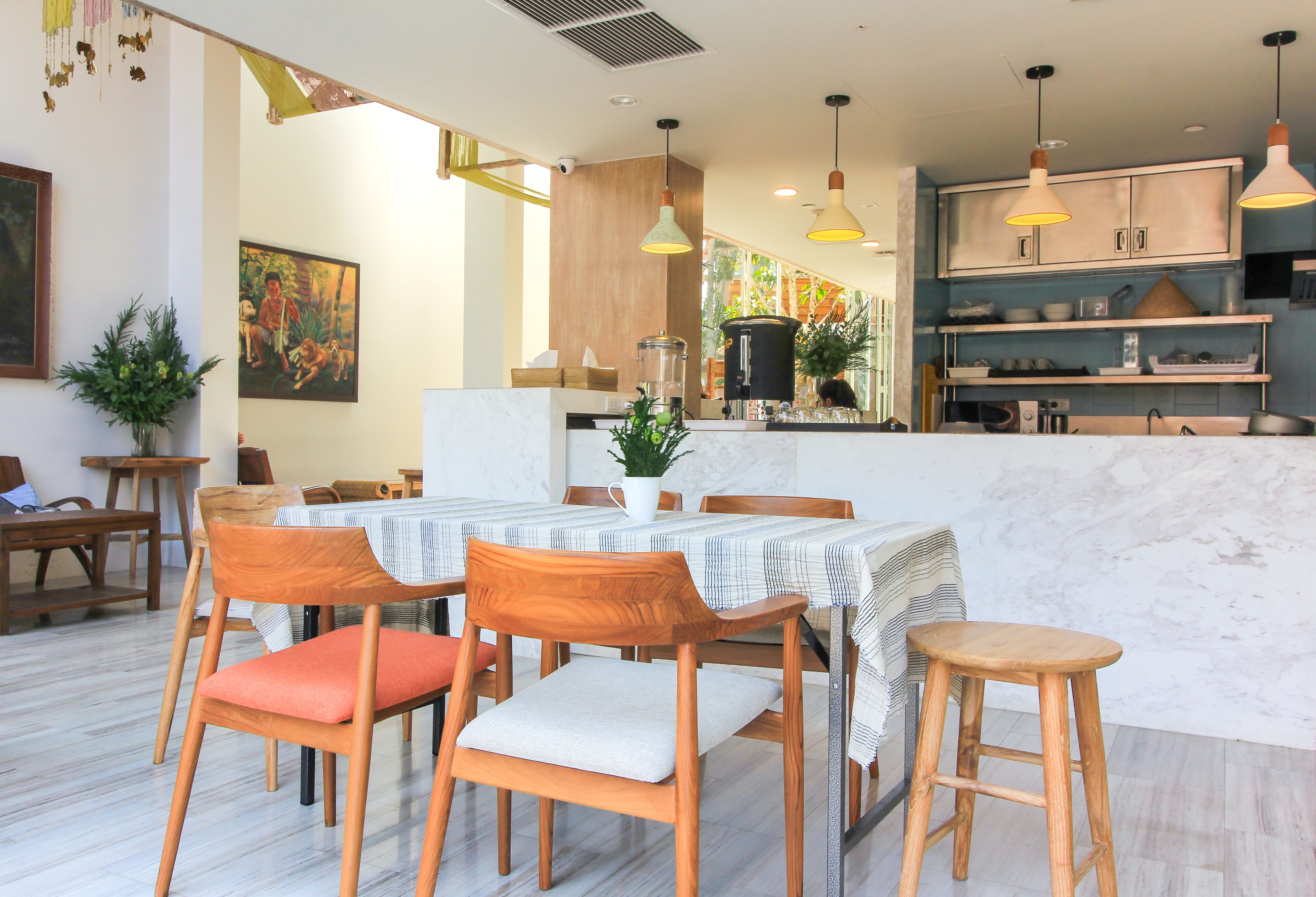 A dining area with wooden chairs and a marble floor, a kitchen with wooden cabinets, and pendant lighting.