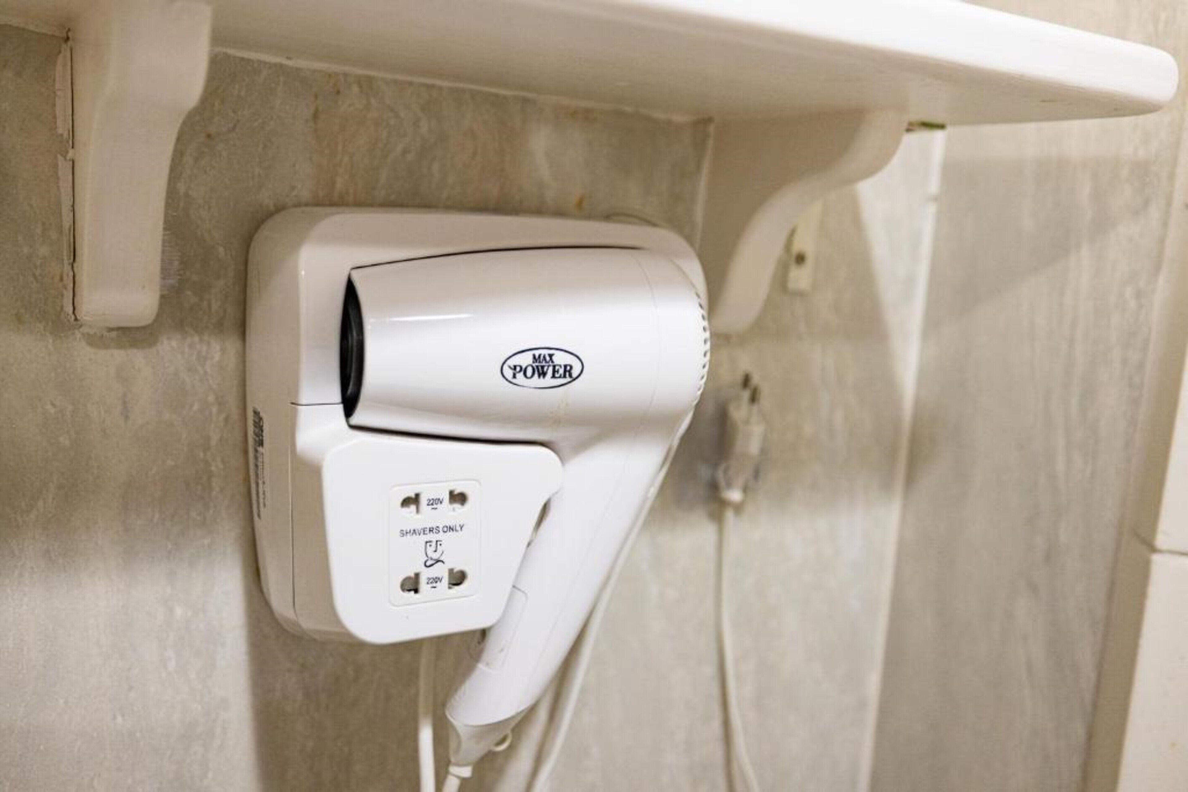 A white hair dryer mounted on a wall with a label indicating it is for shavers only and has a 220V power requirement.