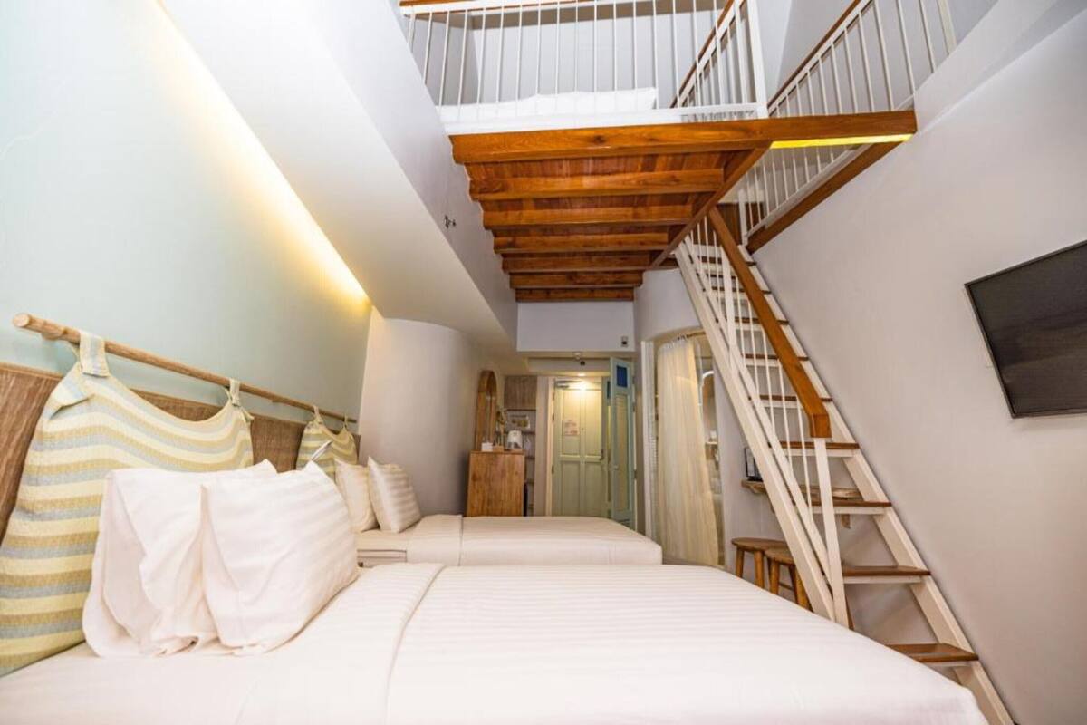 Une chambre avec deux lits, un escalier en bois et une vue sur la cuisine.