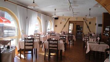 Ein Restaurant mit mehreren Tischen und Stühlen, einem gefliesten Boden und einer gewölbten Decke mit hängenden Lampen.