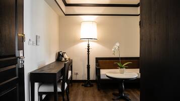 Une pièce comprenant un bureau en bois, une chaise, une table de chevet avec une lampe, une petite table ronde et un lit avec une tête de lit.