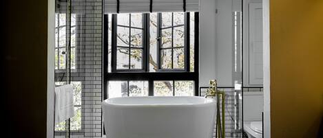 A modern bathroom with a freestanding bathtub, a glass shower enclosure, and a view through a large window.