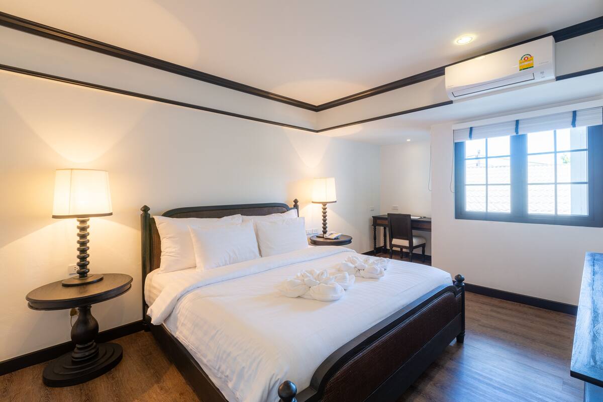 Una habitación de hotel con cama, dos lámparas de noche, un escritorio y un equipo de aire acondicionado.