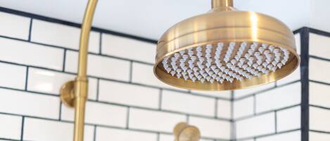 A corner of a bathroom with a gold showerhead and a handheld showerhead against a white tiled wall with black grout.