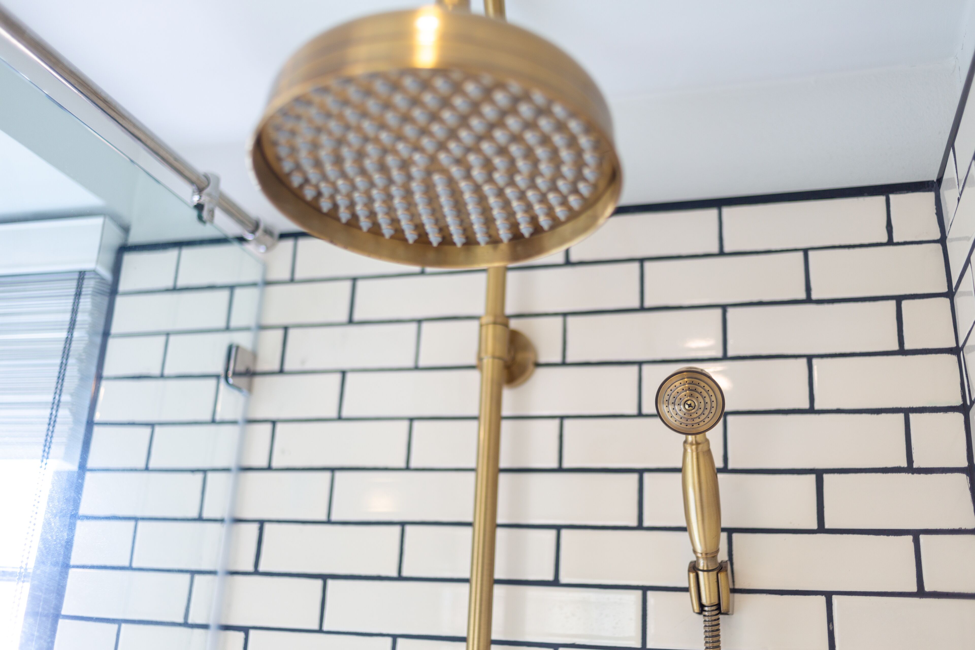 A shower with a gold showerhead and a handheld showerhead against a white and black tiled wall.
