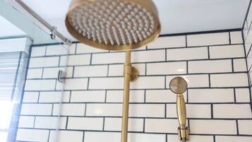 A shower with a gold showerhead and a handheld showerhead against a white and black tiled wall.