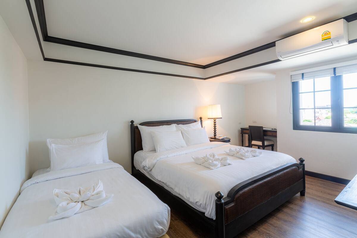 Una habitación de hotel con dos camas individuales, un escritorio, una silla, una lámpara y un equipo de aire acondicionado.