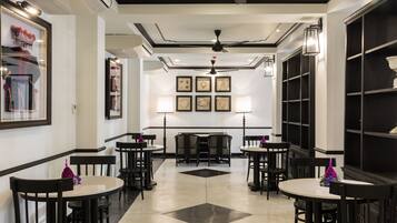 Een hotel lobby met zwart-wit decor, meerdere tafels en stoelen, en ingelijste foto’s aan de muren.