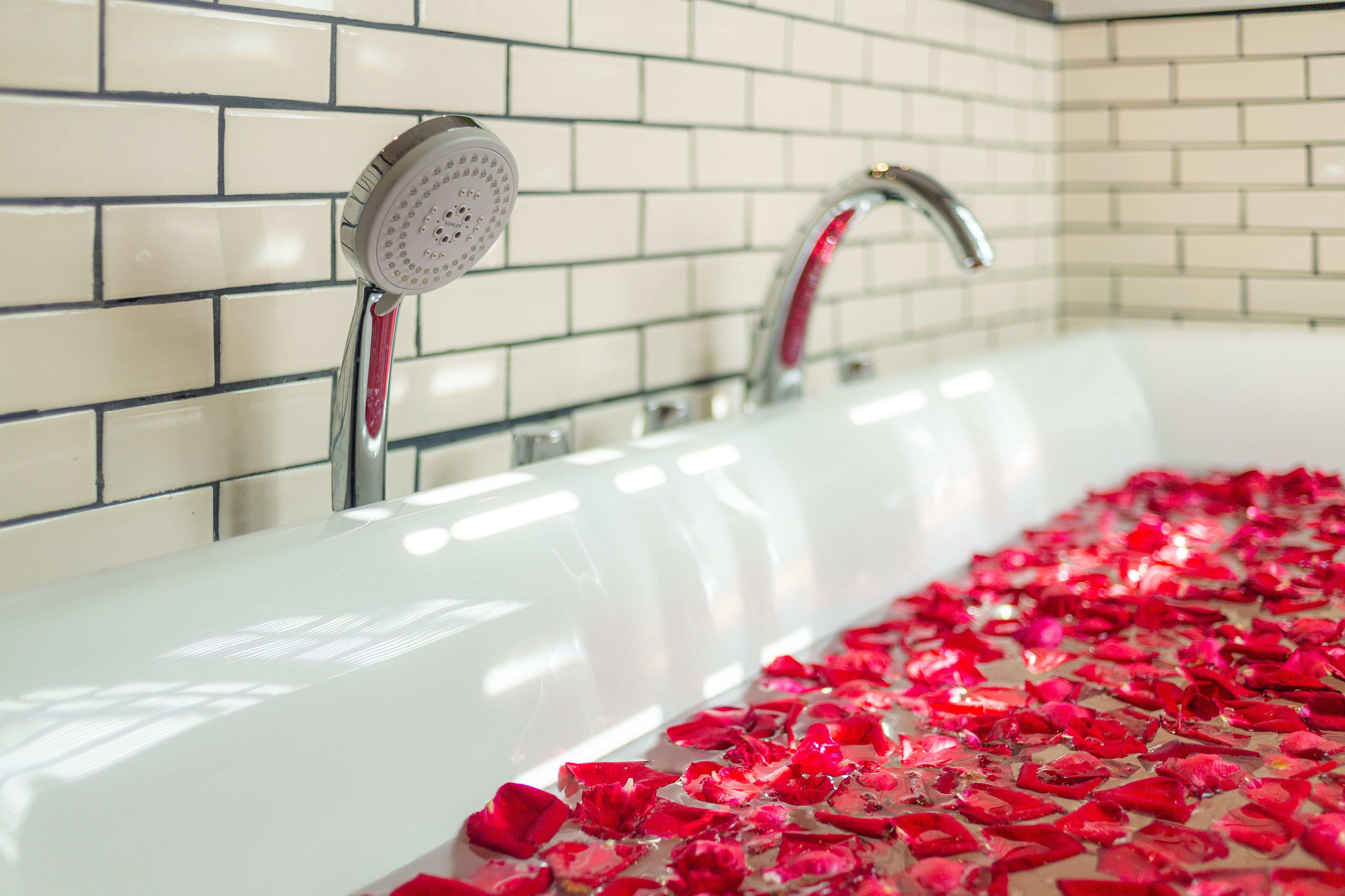 A bathtub with rose petals, a showerhead, and a faucet.