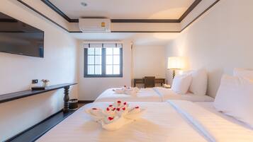 Une chambre d’hôtel avec deux lits, un téléviseur à écran plat, un appareil de climatisation, une fenêtre avec des stores, une table de chevet avec une lampe et une présentation décorative des serviettes.