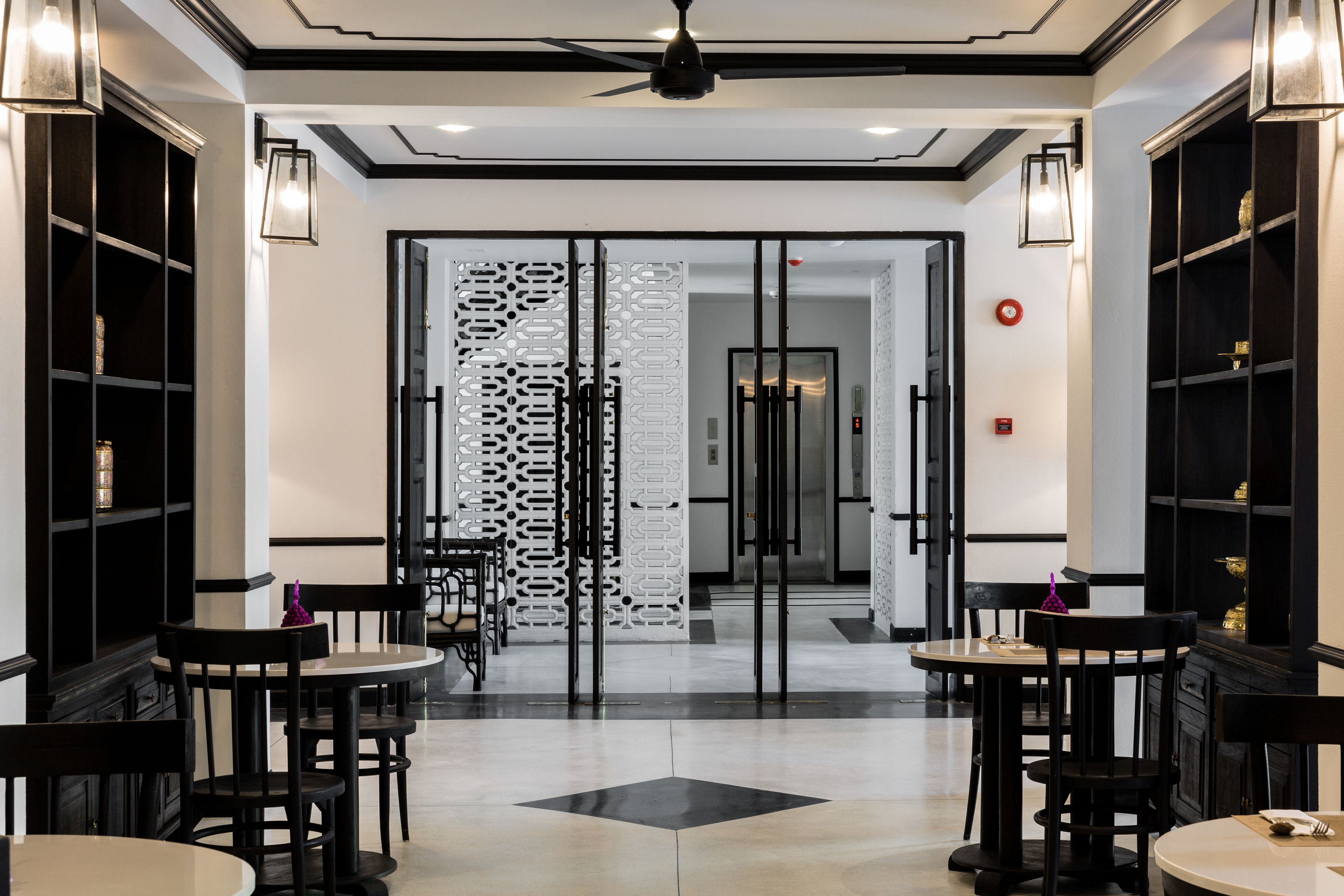 A modern hotel lobby with black and white decor, featuring two round tables and chairs, a decorative wall panel, and a ceiling fan.