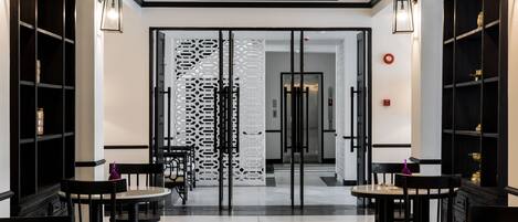 A modern hotel lobby with black and white decor, featuring two round tables and chairs, a decorative wall panel, and a ceiling fan.