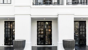 A modern building entrance with two large black doors, a white facade, and two large planters on a tiled floor. - MORA Boutique Hotel (Chiang Rai)