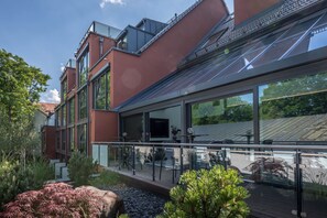 A modern building with large windows, a glass balcony, and a garden area with rocks and plants.