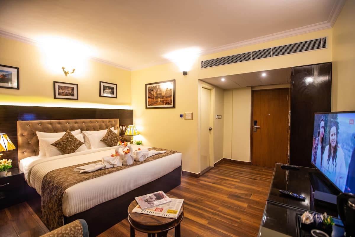 Quarto de hotel com cama grande, televisão, mesinha e porta que dá para outro cômodo.