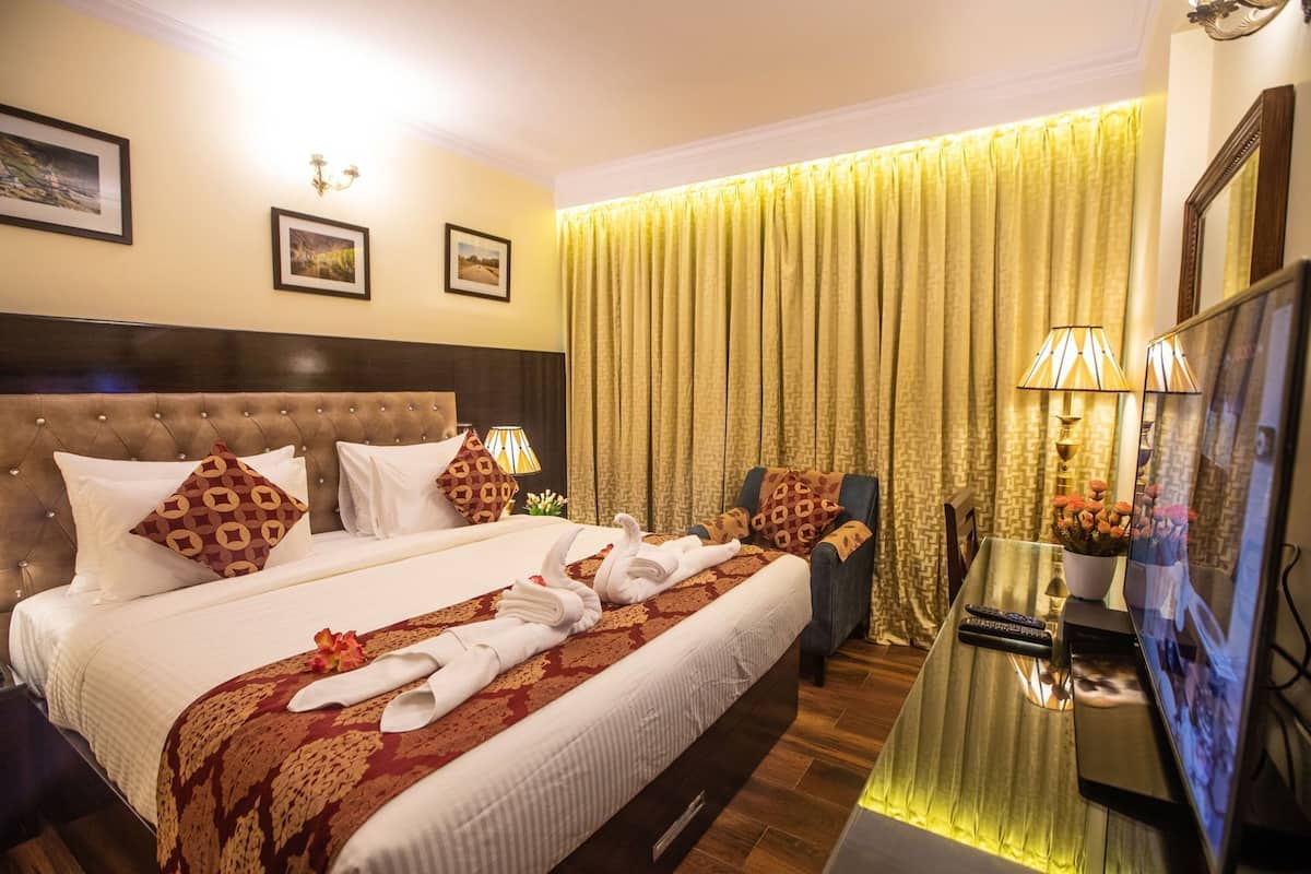 Quarto de hotel com uma cama grande, uma escrivaninha e uma televisão, além de uma cortina.