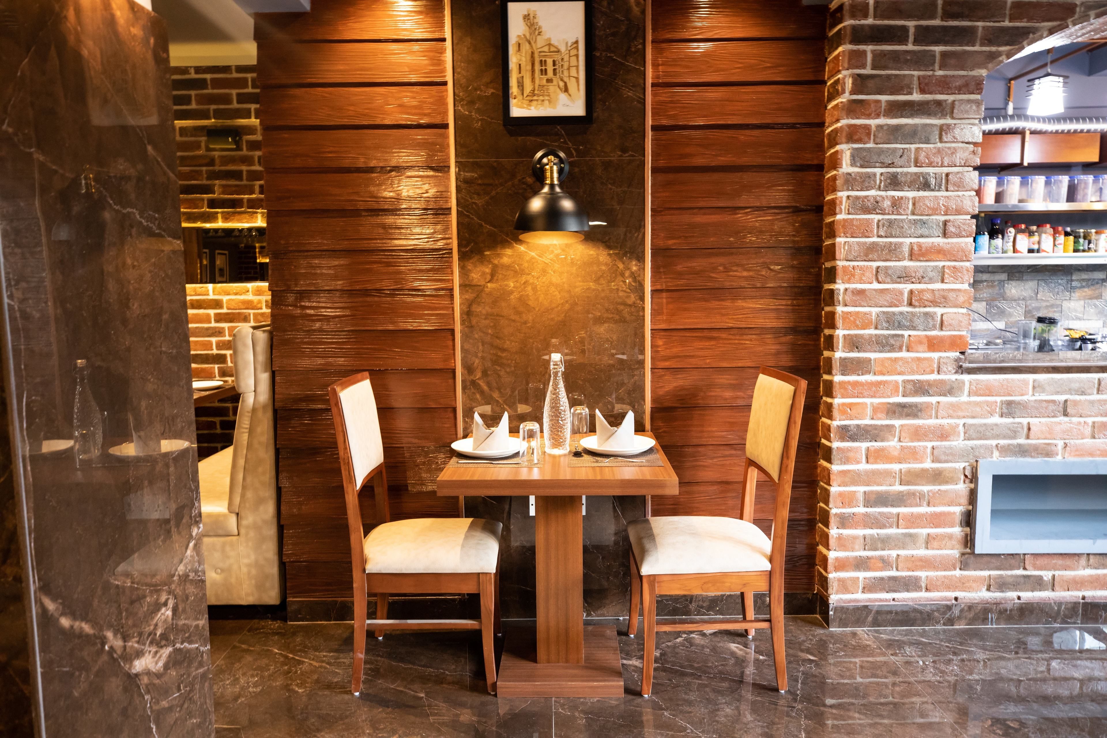 A dining area with a wooden table and chairs, a marble floor, and a brick wall with a shelf of bottles.