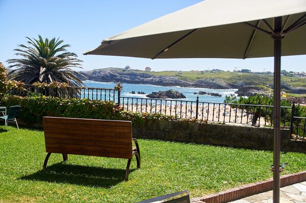 Un banco y una sombrilla con vistas a una playa, costa rocosa y una palmera.