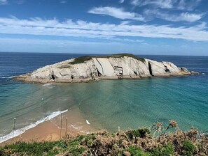 Un paisaje costero con una imponente formación rocosa blanca que se adentra en el mar, aguas azul cristalino y una playa arenosa.