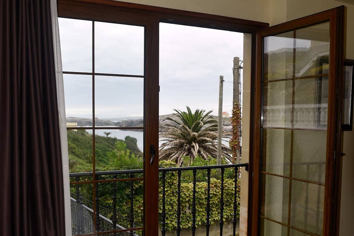 Une chambre dotée d’une grande porte-fenêtre coulissante donnant sur un balcon avec vue sur la mer et la verdure.