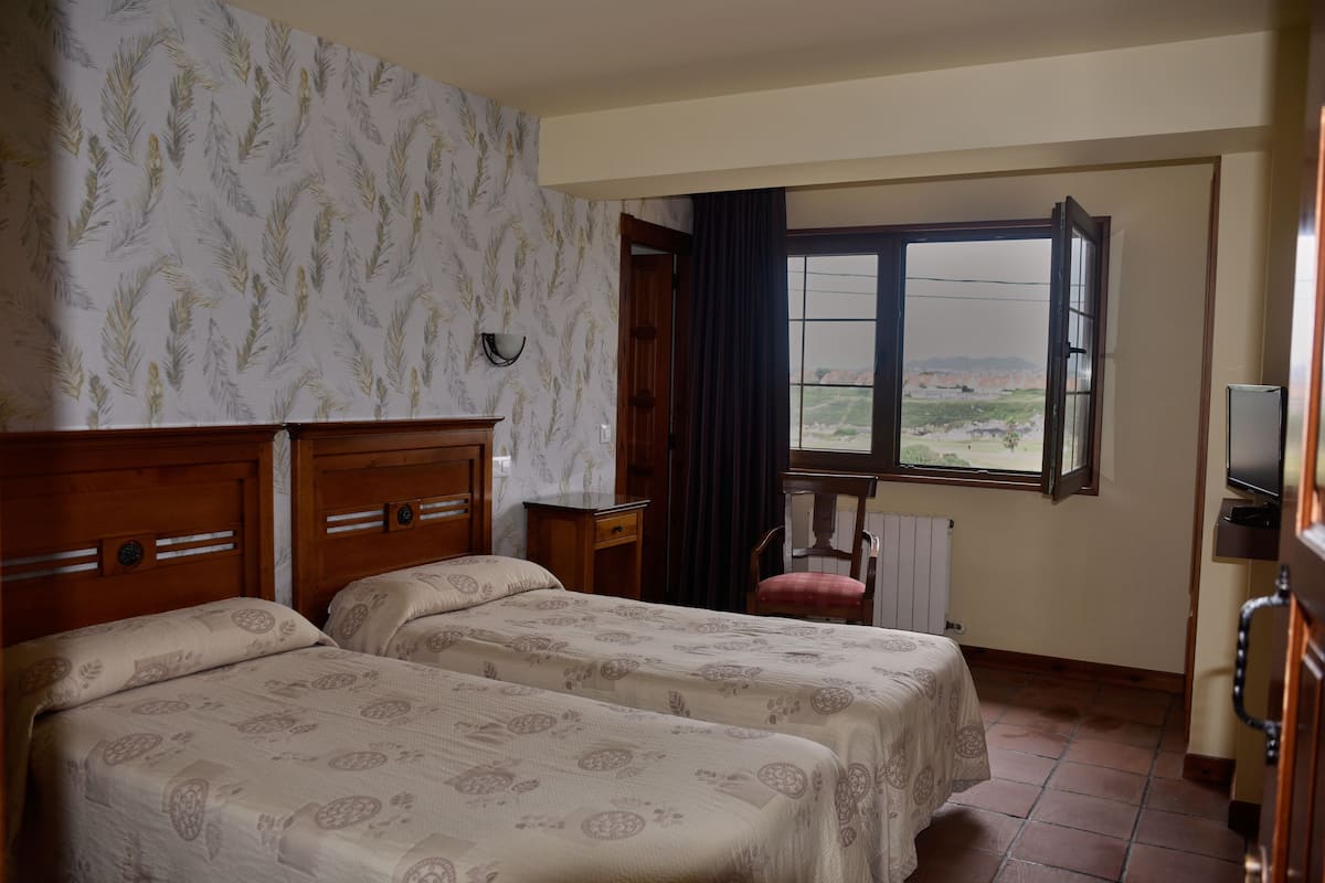 Une chambre d’hôtel avec deux lits, une tête de lit en bois, une fenêtre donnant sur un paysage agréable, une chaise et un téléviseur.