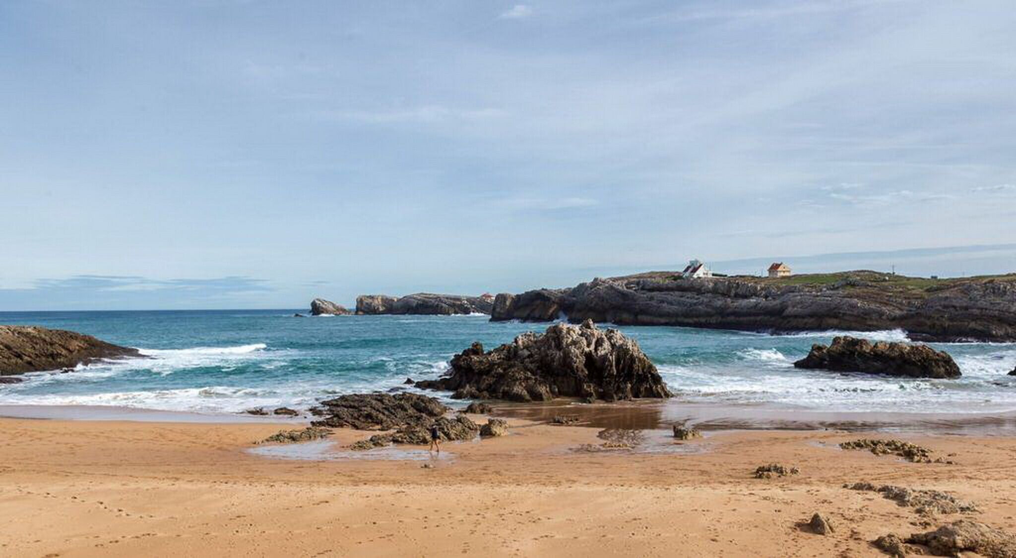 Una playa con afloramientos rocosos y olas tranquilas.