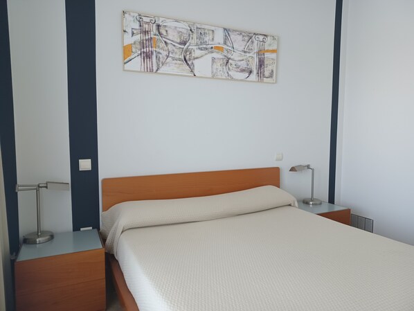Una cama bien hecha con tablero de madera, una lámpara de noche y un cuadro abstracto colgado en la pared.