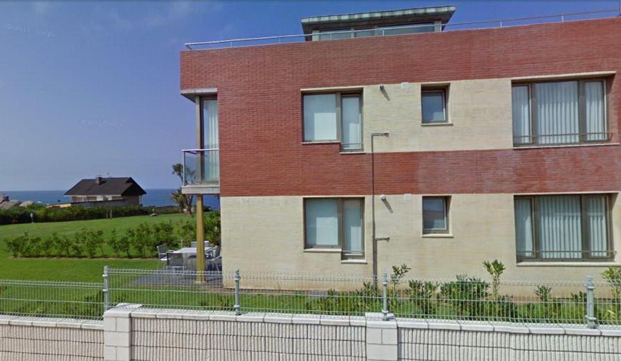 Un edificio moderno de dos plantas con techo plano, amplias ventanas y un balcón visible.
