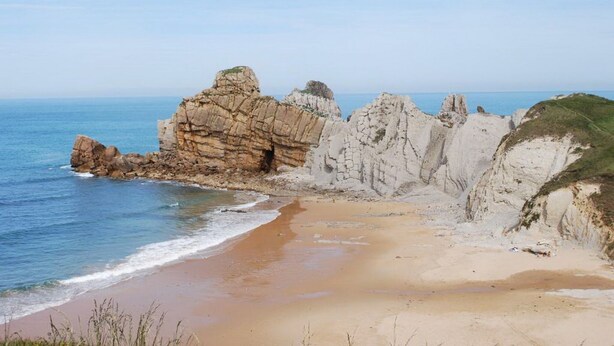 Un paysage côtier avec une plage de sable, des falaises rocheuses et l’océan.