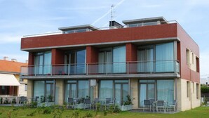 Un bâtiment moderne à deux étages, doté d’un toit plat, de grandes fenêtres et d’un balcon avec des chaises.