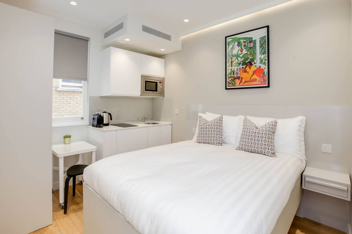 A compact bedroom with a bed, bedside table, and a small kitchenette area.