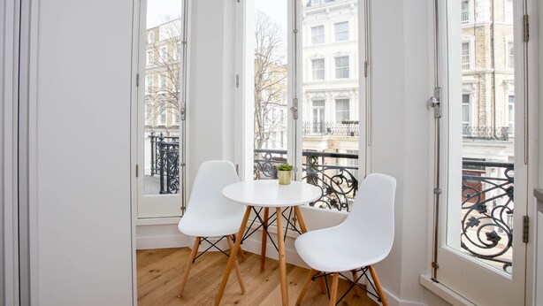 A room with a balcony, white chairs, a small table, and a potted plant. - StayPrime Kensington Serviced Apartments (London)
