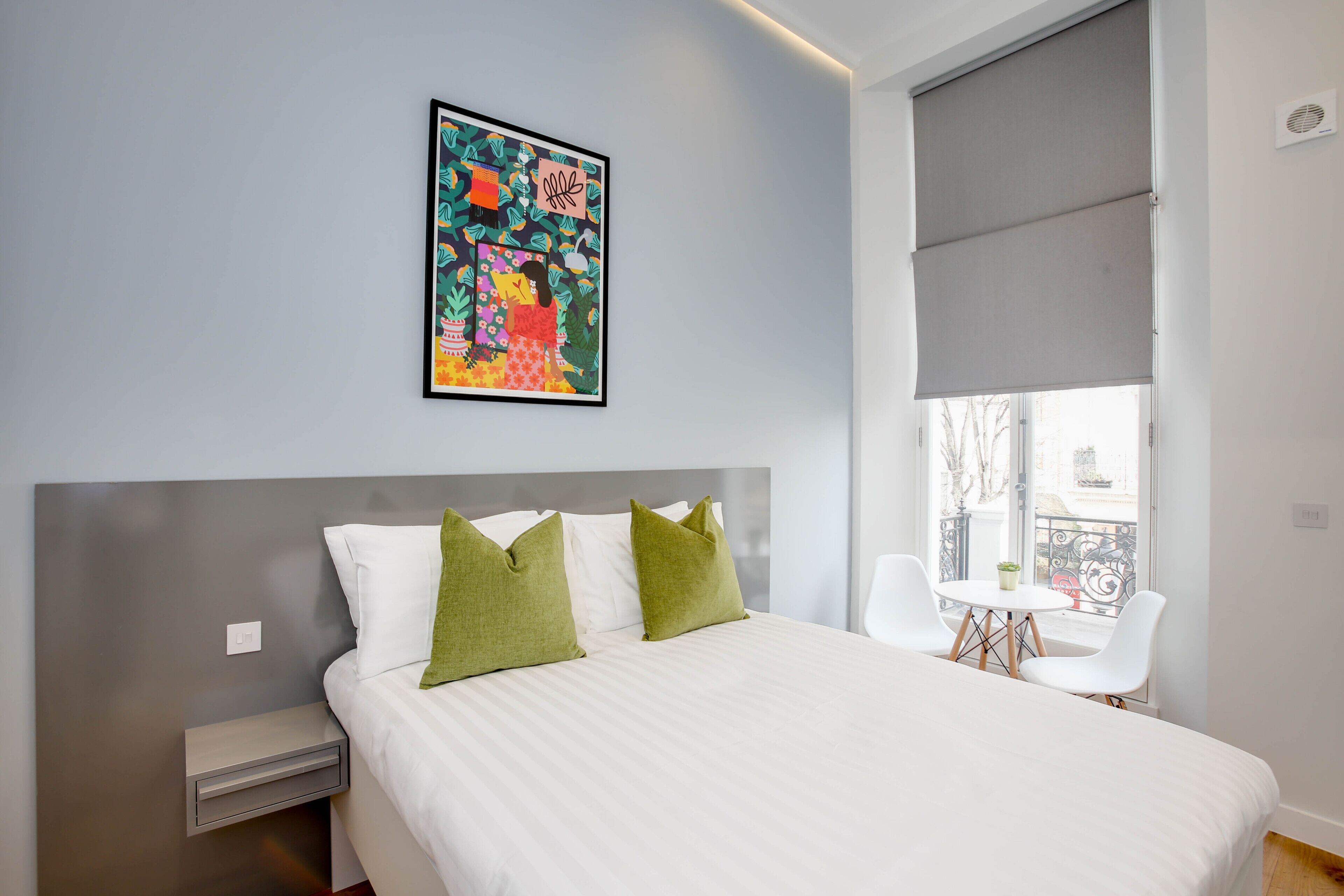 Ein modernes Schlafzimmer mit einem großen Bett, grünen Kissen, einem gerahmten Kunstwerk und einem Balkon mit Tisch und Stühlen.