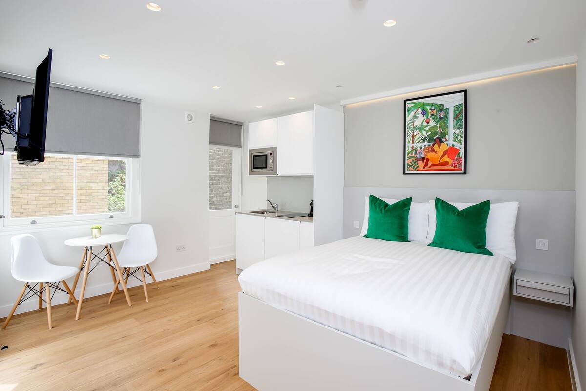 A modern bedroom with a bed, green pillows, a white bedside table, and a wall-mounted TV.