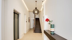 A modern hallway with a staircase, a decorative hanging light fixture, and a vase with red flowers on a console table. - StayPrime Kensington Serviced Apartments (London)