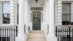 A front view of a building with a central entrance, white columns, a black metal fence, and a green door with a number above it. - StayPrime Kensington Serviced Apartments (London)