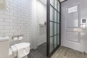 A bathroom with white tiled walls, a toilet with a towel, a glass shower enclosure, and a door with a sign. - Moju Hotel Shanghai (Shanghai)