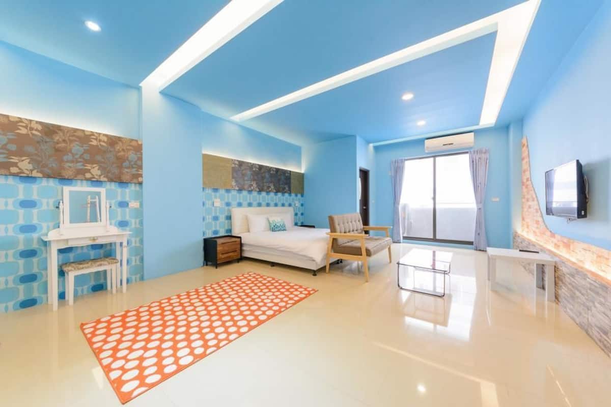 A modern bedroom with a bed, a chair, a desk, and a TV.