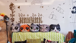 A bed with a green and white checkered bedspread, multiple cat-themed pillows, and a wall with Christmas decorations. - Cat Mia Hostel (Hualien City)
