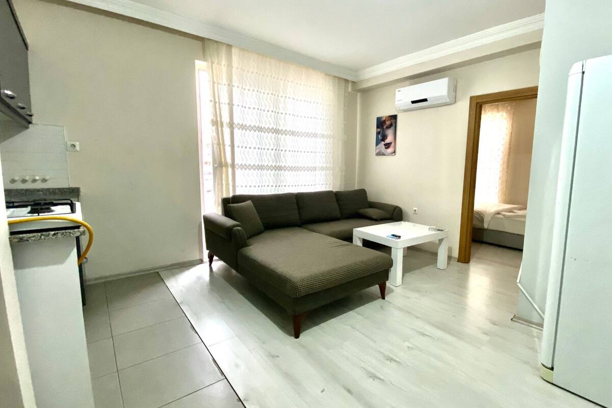Um espaço compacto com sofá, uma mesinha, frigorífico e cozinha equipada com fogão e forno.